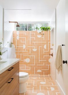 a bathroom with an orange and white tiled wall next to a sink, toilet and window