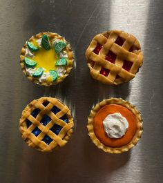 four small pies with different toppings sitting on top of a metal countertop