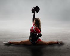 a female cheerleader sitting on the ground with her arms in the air and holding a pom - pom