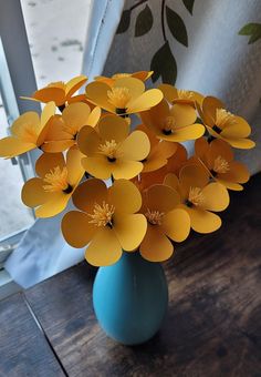 a blue vase filled with yellow flowers sitting on top of a wooden table next to a window