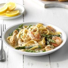 a plate of pasta with shrimp, asparagus and lemon slices on the side