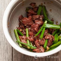 a bowl filled with meat and green beans on top of a wooden table next to a fork