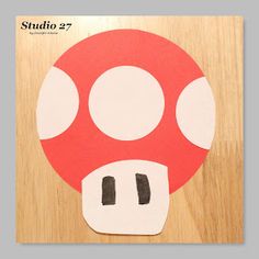 a red mushroom cut out on top of a wooden surface with the word studio 27 written below it