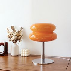 an orange lamp sitting on top of a wooden table next to a vase with flowers