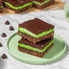 three pieces of chocolate and green dessert on a plate with mints around it,