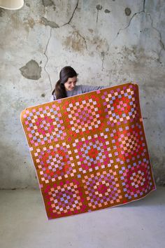 a woman holding up a quilt in front of a wall