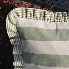 a green and white striped pillow sitting on top of a wooden bench next to shrubbery