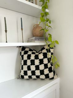 a black and white pillow sitting on top of a shelf next to a potted plant