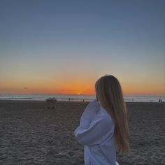 a woman standing on top of a sandy beach next to the ocean at sun set