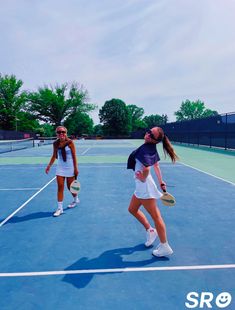 two women are playing tennis on a blue court with trees in the backgroud