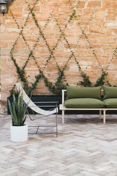 two green couches sitting next to each other in front of a stone wall with ivy growing on it