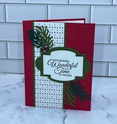 a red and white christmas card with pine branches on it, sitting on a marble surface