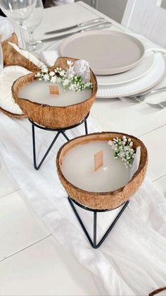 two coconut shell bowls with flowers in them are sitting on a table set for dinner