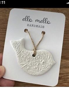 a hand holding a white ceramic bird pendant on a card that says, elo mela handmade