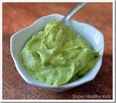 a white bowl filled with green guacamole on top of a wooden table