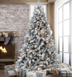 a white christmas tree in front of a fireplace with presents under it and stockings on the floor