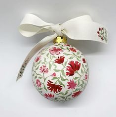 a white ornament with red and green flowers on it's ribbon tied around the top