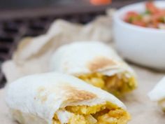 two burritos cut in half sitting on a table next to a bowl of salsa