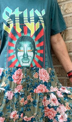 a man standing next to a brick wall wearing a t - shirt and floral skirt