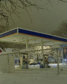 a gas station with snow on the ground and trees in the background at night time