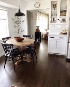 a dining room table and chairs in front of an open kitchen area with white cabinets