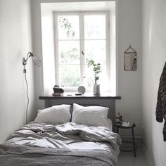 a bed sitting under a window next to a wooden table with a lamp on it