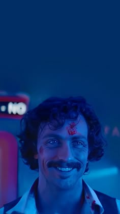 a man with blood on his face smiling at the camera in front of a neon sign