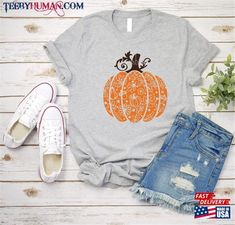 a t - shirt with an orange pumpkin on it next to ripped jeans and sneakers