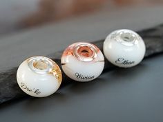 three white and gold glass beads with names on them sitting on a piece of wood