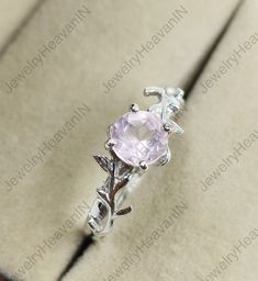 an engagement ring with a pink stone in the center and leaves around it, sitting on top of a box