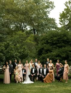 a large group of people in formal wear posing for a photo on the grass with trees in the background