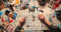 a person writing on top of a book surrounded by art supplies and other things that are scattered around