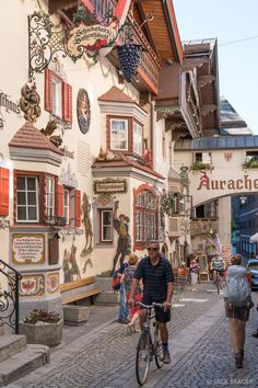 a man riding a bike down a cobblestone street in front of buildings with red shutters