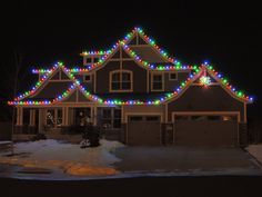 a house with christmas lights all over it's roof and garage doors in front of it