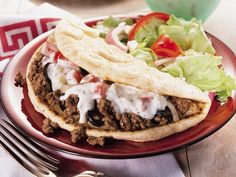 a taco sandwich on a red plate with lettuce and tomato wedges