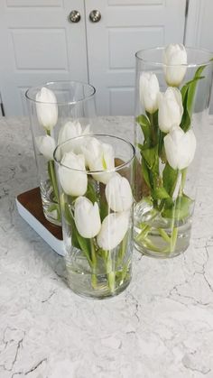 two clear vases with white flowers in them on a marble counter top next to a door