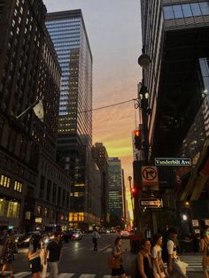 people crossing the street in front of tall buildings at sunset or dawn with traffic lights