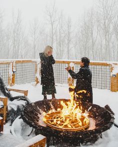 two people standing around a fire pit in the snow