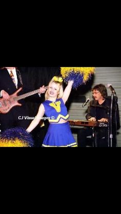 a woman in a blue dress is holding her arms up while standing next to a guitar