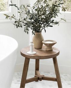 a potted plant sitting on top of a wooden stool next to a bath tub