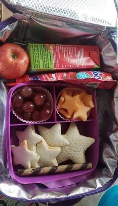 an open lunch bag filled with fruit and snacks, including crackers, apples, cheese, and star shaped cookies