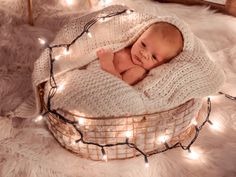 a baby wrapped in a blanket is laying on top of a basket with christmas lights around it