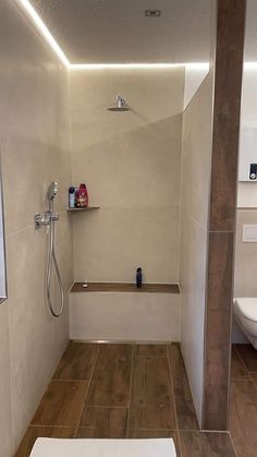 a white toilet sitting next to a walk in shower under a light brown wooden beam