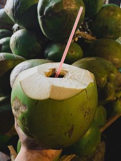 a person holding a green coconut with a straw in it's mouth and some other fruit behind them