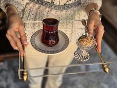 a woman holding a tray with a cup and spoons on it, next to a glass dish