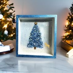 a small christmas tree in a blue frame on a table next to a decorated christmas tree