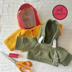 the doll is wearing a green jacket and pink hoodie with scissors next to it