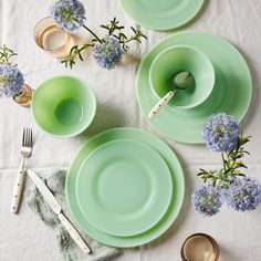 the table is set with green plates, silverware and blue hydrangea flowers