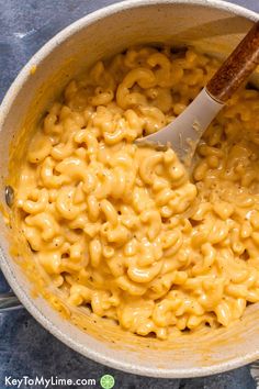 macaroni and cheese is being stirred in a large pot with a wooden spoon