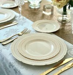 the table is set with white plates and gold cutlery, silverware, and flowers in vases